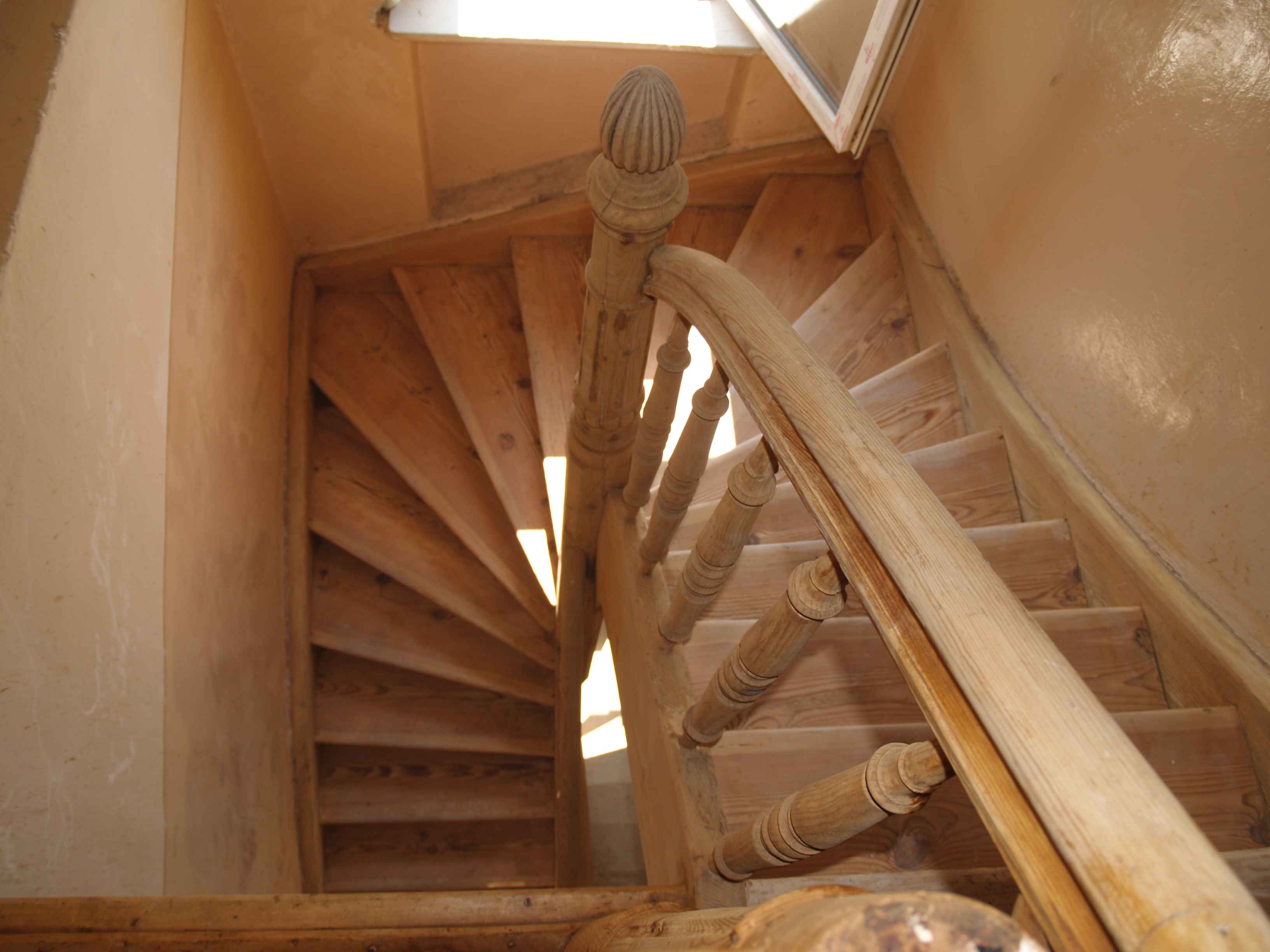 Spiralne, drewniane schody z toczonymi balustradami, widoczne z góry, z naturalnym oświetleniem wpadającym przez okno na górze.